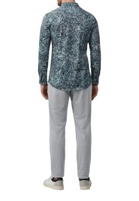 Chemise à manches longues en bleu sarcelle avec un motif florale, assortie à un pantalon de survêtement gris clair et des baskets blanches. La chemise possède un col.