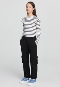 Pasy z długim rękawem z falbanami, zestawione z czarnymi spodniami cargo z bocznymi kieszeniami. Obuwie: jasnoniebieskie trampki.