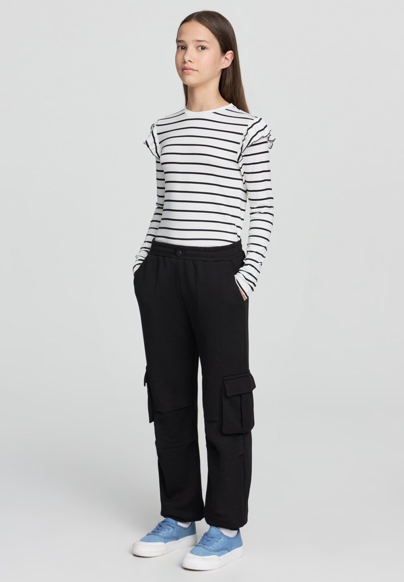 Pasy z długim rękawem z falbanami, zestawione z czarnymi spodniami cargo z bocznymi kieszeniami. Obuwie: jasnoniebieskie trampki.