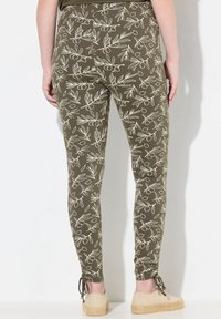 Leggings verde oliva con un motivo di foglie e bacche bianche, realizzati in un tessuto elastico, design aderente e dettagli con cordini alla caviglia.