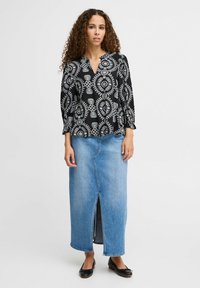 Blusa nera con motivi floreali bianchi, scollatura a V e maniche a sbuffo. Abbinata a una gonna maxi in denim blu con uno spacco frontale. Ballerine nere.