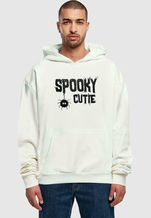 Hvid hoodie lavet af blødt stof med et "Spooky Cutie" grafisk tryk i sort med detalje af en edderkop. Inkluderer en kængurulomme og ribbede manchetter.