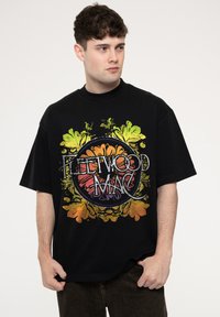 Black oversized t-shirt featuring a colorful floral design and "FLEETWOOD MAC" text in a vintage style. Soft cotton material.