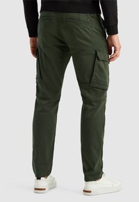 Donkergroene cargobroek met meerdere zijzakken, een slim fit design en een gladde stoffen textuur, gecombineerd met witte sneakers.
