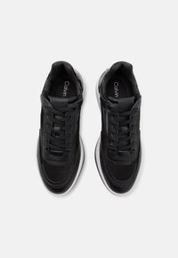 Černé tenisky kombinující hladkou kůži a textil, se zaoblenými tkaničkami, polstrovanými podrážkami a nenápadným logem na jazycích.