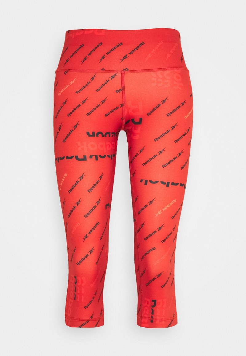 Červené capri legíny vyrobené z elastického materiálu, zdobené opakujícím se černým vzorem loga Reebok. Vysoký pás pro zvýšenou podporu.