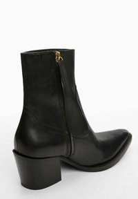 Mustat nahka nilkkurit, joissa on terävä kärki, sivuvetoketju kultaisella yksityiskohdalla ja paksu musta korko. Sujuva pinta vähäisillä ompeleilla.