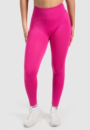 Roze high-waisted legging met een geribbelde textuur, ontworpen voor een aangesloten look, gecombineerd met witte sportschoenen.