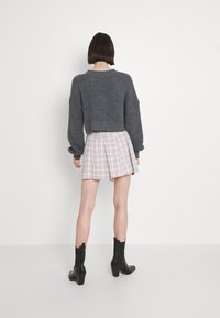 Grauer cropped Pullover, karierter plissierter Rock in Pastellfarben, schwarze Absatzstiefel. Strukturiertes Material auf dem Pullover, glatte Oberfläche des Rocks.