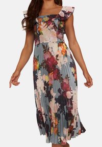 Kukallinen printtimekko röyhelöillä koristelluilla olkaimilla, laskostettu hame, jossa sinisen, vaaleanpunaisen ja punaisen sävyisiä kukkia, jäsennelty yläosa.