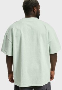 Tricou supradimensionat de culoare verde menta, fabricat din bumbac, cu guler rotund, mâneci scurte și o croială lejeră, având o textură moale.