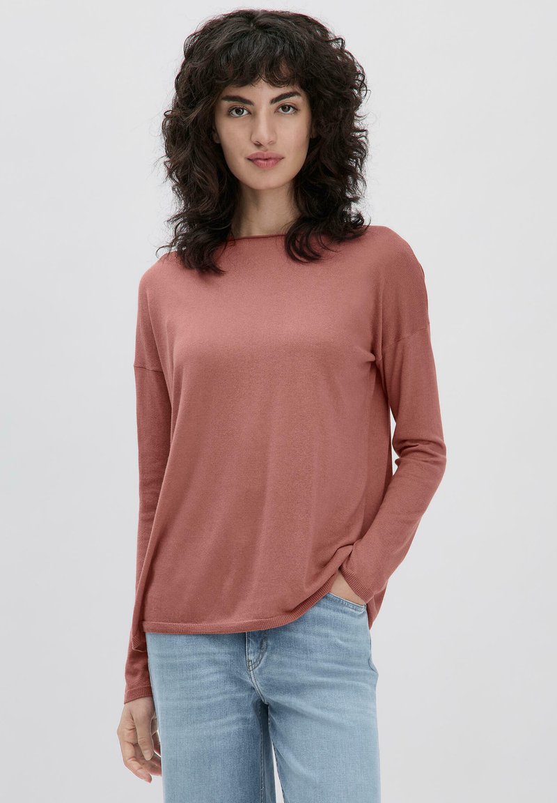 Langärmliges, mauves Oberteil mit lockerer Passform, rundem Ausschnitt und weicher Textur. Kombiniert mit hellblauen Jeans. Dezente Seitennahtdetails.