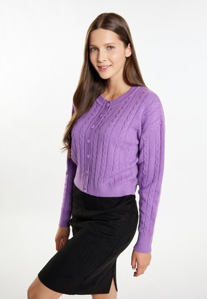 Cárdigan de punto trenzado morado con cuello redondo y cierre de botones, combinado con una falda negra ajustada, que captura texturas suaves y un color vibrante.
