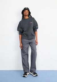 Kullsvart genser med puffede ermer, med en liten logo. Kombinert med løse grå cargo-bukser og svarte sneakers. Bøttehatt fullfører antrekket.