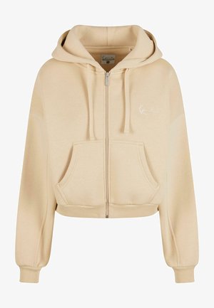 Beige színű cropped zipzáros kapucnis pulóver, húzózsinórral, elülső zsebekkel és puha textúrával. Diszkrét logó hímzés található a mellrészen.