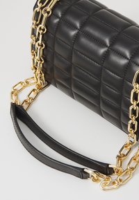 Schwarze, gesteppte Lederhandtasche mit einer goldenen Kettenriemen und einem schwarzen Lederobergriff, der eine glatte Textur und einen glänzenden Finish aufweist.