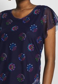 Navy blue top with floral patterns in vibrant colors. Features translucent sleeves and a scoop neck design, made from soft, lightweight fabric.
