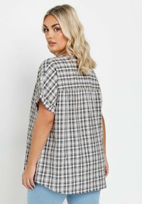 Camicia a maniche corte a quadri in grigio e bianco con un fit rilassato, presenta dettagli arricciati sulla parte posteriore e un orlo curvo.