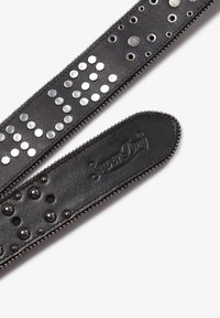 Schwarzer Lederarmband mit silbernen Nieten und Beschlägen sowie einer strukturierten Oberfläche. Logo auf einer Seite geprägt. Glatte Kanten mit Nieten.