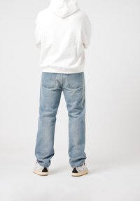 White hoodie, light blue jeans, and grey sneakers. Hoodie has a hood; jeans are slightly loose with a faded finish. Sneakers feature black accents.