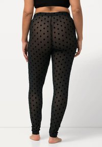 Schwarze Leggings mit Polka-Dots in transparenter Optik, ausgestattet mit einem figurbetonten Bund und schmal zulaufenden Beinen, die eine glatte und leichte Textur zeigen.