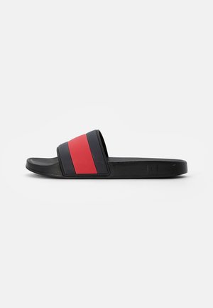 Sandale à enfiler noire avec une large bride rayée noire et rouge et une semelle texturée, vue de côté sur fond blanc.