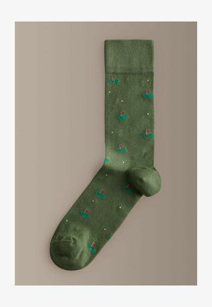 Zelená ponožka s malými motívmi golfových jamiek obsahujúcimi červené zástavky a biele golfové loptičky rozptýlené po tkanine.