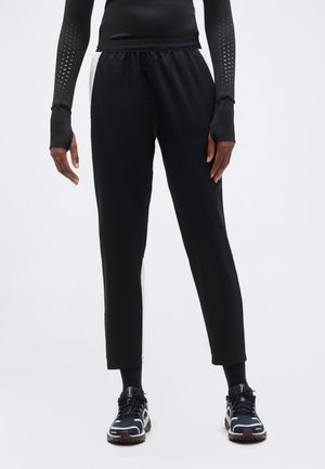 Person wearing black tapered pants with white side panels, black long-sleeve top with thumb holes, black socks, and black athletic shoes.