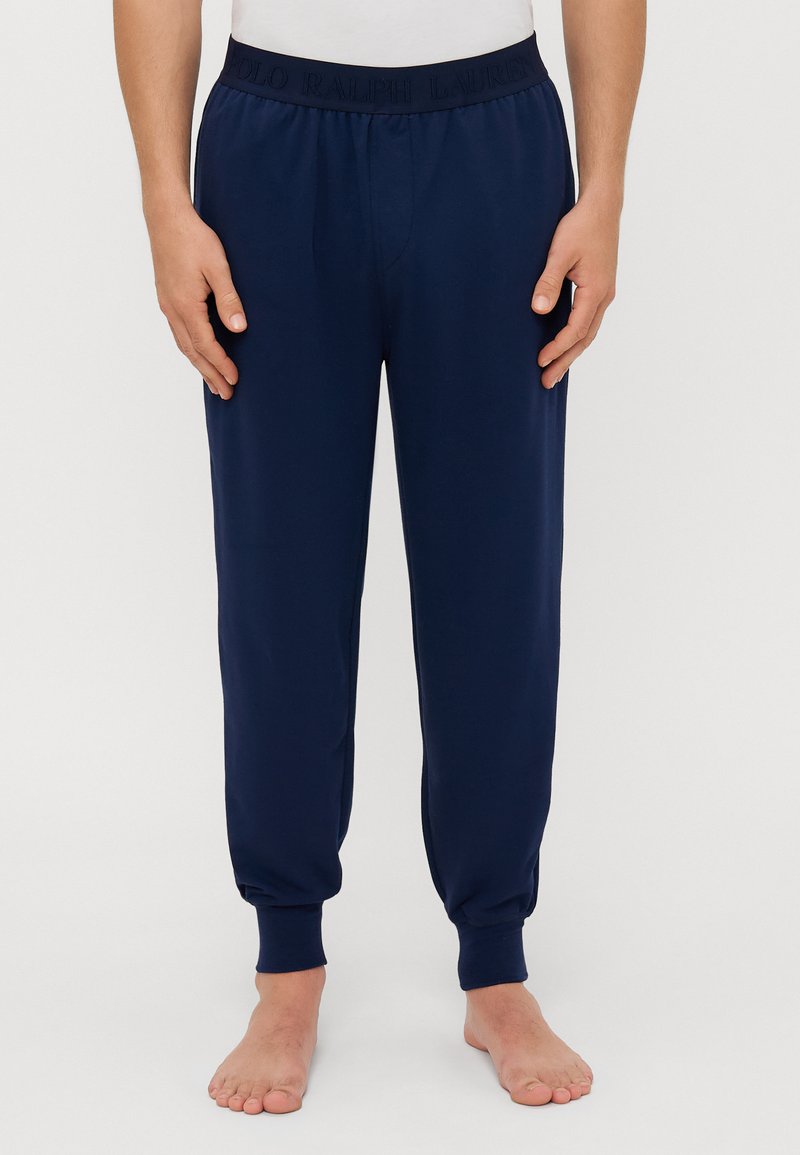 Tamno plave jogger hlače s elastičnim pojasom na kojem je utisnuto "Polo Ralph Lauren". Suženi kroj s manžetama, izrađene od mekog materijala.