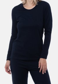 Marinblå långärmad topp i mjukt material med rund halsringning och åtsittande design, bärs med matchande mörka byxor.