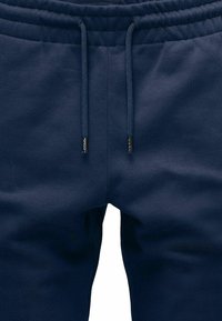 Marineblaue Jogginghosen aus einem weichen, dehnbaren Stoff mit einem Bund, der über einen Kordelzug verfügt. Metallakzente an den Enden des Kordelzugs.