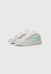 Zemu zemu balti un pelēki sporta apavi ar baltām auklām un katrā pusē zaļā kontūrā Nike svītra.