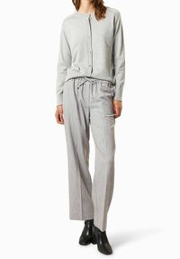 Cardigan gris clair avec fermeture à boutons, associé à un pantalon large rayé clair et des bottines à talons noires. Texture du tissu douce.