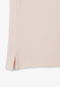 Ljusrosa polo skjorta med strukturerad textil, sidsprund i fållen och sydda detaljer. Enkelt design med klassisk krage.