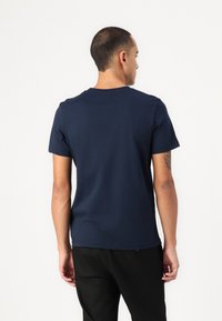 T-shirt en coton bleu marine avec un col rond, des manches courtes et une texture lisse, vue de l'arrière. Aucun motif ni accent visible.