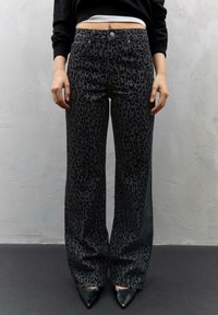 Visoko pasovi, široke hlače iz temno sive tkanine s črno leopardjo vzorcem. Tkanina se zdi gladka z diskretnim sijajem; ima pet žepov.