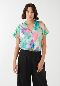 Kortærmet bluse i flerfarvet blomsterprint med grønne, pinke og blå nuancer; v-hals design; sammen med sorte bukser med elastisk talje.