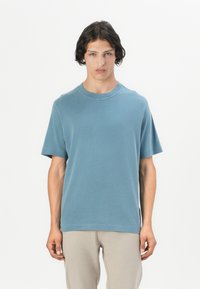 Tricou cu mânecă scurtă și gât rotund, în nuanță de albastru stins, fabricat dintr-un material moale. Prezintă o croială lejeră, cu cusături fine și fără modele vizibile.