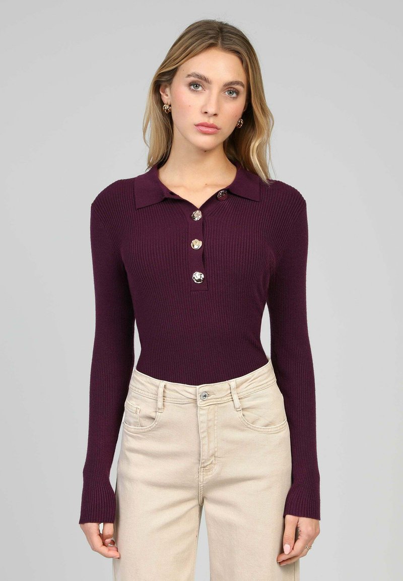 Haut long à manches longues côtelé couleur prune avec col et quatre gros boutons. Associé à un jean taille haute beige clair, il présente une coupe décontractée.