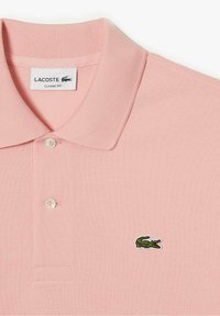 Polo rosa avec une coupe classique, featuring un tissu texturé, trois boutons, et un logo de crocodile brodé vert sur la poitrine.