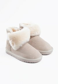 Bottes de cheville beiges en daim avec une douce bordure en fausse fourrure blanche. Bout arrondi, semelle plate avec un motif texturé et des détails cousus.