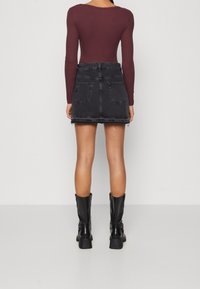 Svart denim mini kjol med fransad nederkant, två bakfickor, bärs med en tight maroon långärmad topp och svarta klackstövlar.