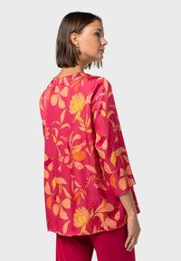 Top de manga corta en fucsia con un estampado floral en tonos naranjas y amarillos, confeccionado en una tela suave y con un corte holgado.