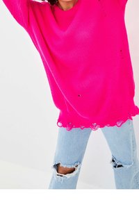 Fuchsia knit sweater with a relaxed fit, featuring distressed edges and a V-neck. Paired with light blue ripped jeans.