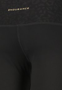 Musta leggingit, joissa on tiukka malli ja jotka on valmistettu joustavasta materiaalista. Lahkeiden yläosassa on hillitty leopardikuvio ja kultainen logo.