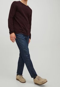 Pull à manches longues bordeaux, jean en denim bleu, et chaussures en daim marron clair avec lacets. Design simple, texture douce, et coupe décontractée.