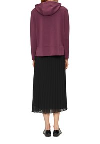 Paarse hoodie met een aangehechte capuchon, gecombineerd met een zwarte plissé rok. De outfit wordt aangevuld met zwarte schoenen met een glanzende afwerking.