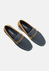 Zapatos de tela azul marino sin cordones con acentos en marrón, cuero texturizado, costuras en contraste y cordones decorativos en marrón sobre una suela blanca.