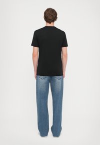 T-shirt preta de manga curta combinada com jeans de perna larga azul claro, apresentando uma silhueta simples e detalhes de costura padrão.