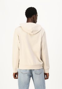 Haut à capuche beige avec un cordon de serrage, des poignets et un ourlet côtelés, associé à un jean en denim bleu clair. Texture douce, design simple, sans motifs visibles.